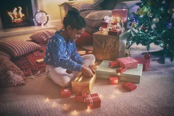 クリスマスに彼女の居間の床に座って 笑顔とプレゼントを開く若い混合レースの女の子の側面図 — ストック写真