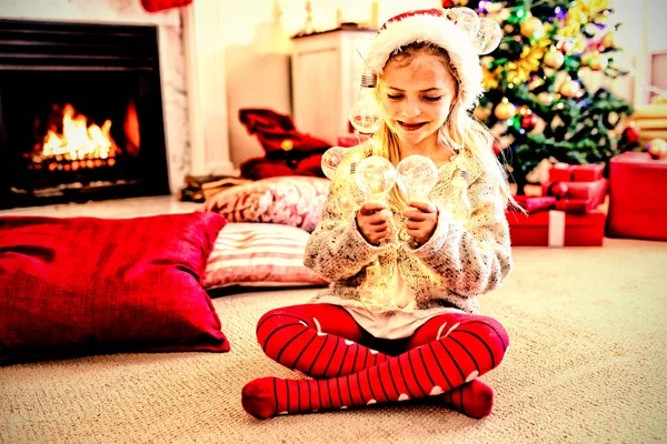 圣诞节时 一个快乐的年轻白种女孩戴着圣诞老人的帽子 在客厅里拿着仙女灯 — 图库照片