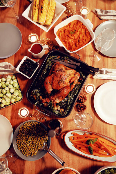 Вид сверху на жареную индейку, овощи, тарелки и свечи на праздничный стол дома
