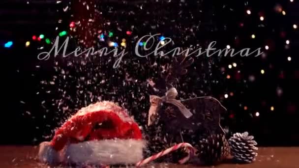 雪の結晶が降る白い文字で書かれた単語メリークリスマスのアニメーション サンタの帽子の前で 松のコーンとトナカイ — ストック動画