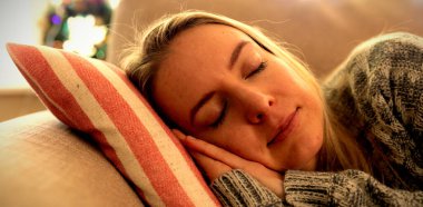 Oturma odasında kanepede uyuyan gülümseyen genç beyaz bir kadının ön görünümü