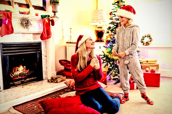 一个年轻的白人女人坐在地板上 身边站着她的小儿子 圣诞节的时候 两个人都戴着圣诞帽坐在客厅里 一边笑一边说话 — 图库照片