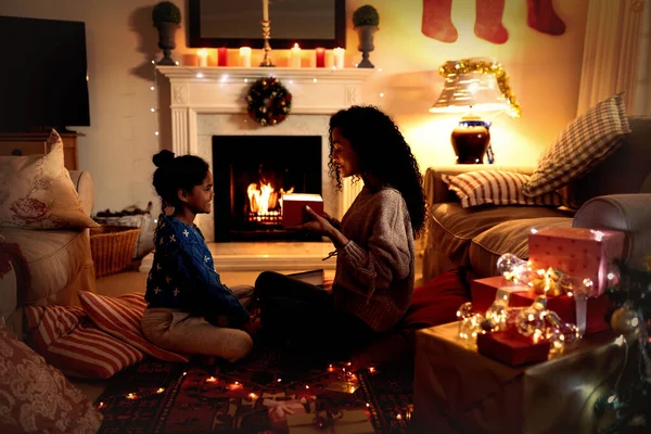 크리스마스에 자신의 거실에서 그녀의 바닥에 여성의 측면보기 미소와 선물을주는 — 스톡 사진