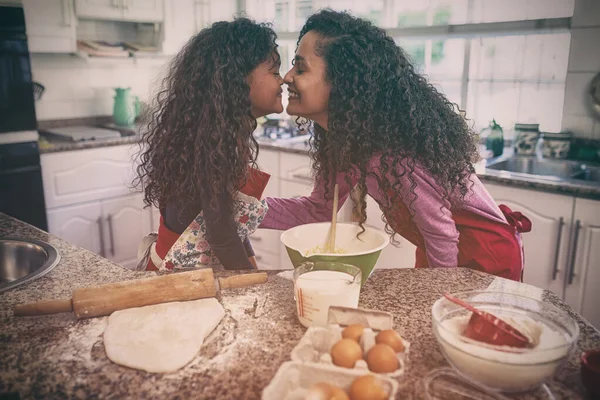 Side view of a mixed race woman in a kitchen with her young daughter at Christmas, making cookies, facing each other and touching noses