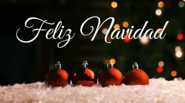 Kırmızı Noel süsleri ve arka planda yanıp sönen ışıkların üzerine bembeyaz yazılmış Feliz Navidad kelimelerinin animasyonu