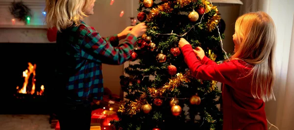 若い白人の兄弟姉妹がクリスマスの時期に居間にクリスマスツリーを飾る側面図 — ストック写真