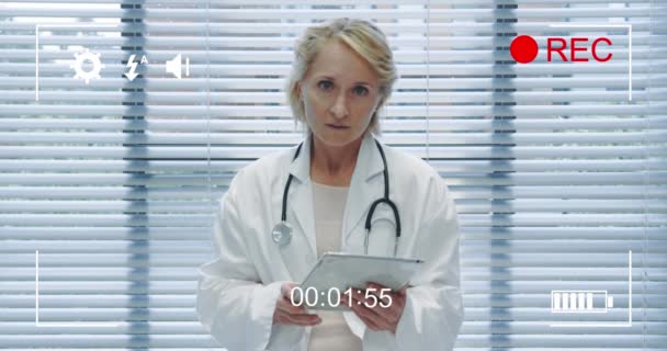 用图标和定时器4K在数码相机的屏幕上拍摄的中年白人女医生手持平板电脑和说话的肖像的动画 — 图库视频影像