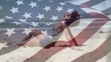 Sahilde güneşlenen melez bir kadının üzerinde Amerikan bayrağının dalgalanması. Amerika Birleşik Devletleri bayrağı ve tatil konsepti dijital kompozisyon