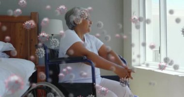 Tekerlekli sandalyede oturan, pencereden dışarı bakan yaşlı melez kadının üzerinde süzülen makro Covid-19 hücrelerinin animasyonu. Coronavirus Covid-19 pandemik konsept dijital bileşik