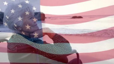 Sahilde tekerlekli sandalyede oturan yaşlı beyaz bir kadının üzerinde Amerikan bayrağının dalgalanması. Amerika Birleşik Devletleri bayrağı ve tatil konsepti dijital kompozisyon