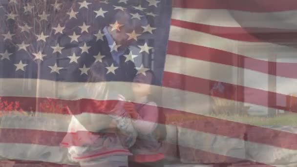 祖父の娘を抱えるアジア系男性に手を振っているアメリカ国旗のアニメーション 米国の国旗と休日のコンセプトデジタル組成物 — ストック動画