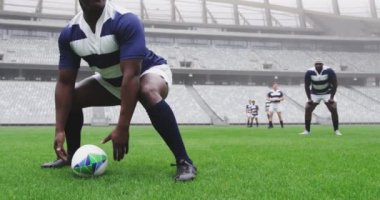 Kamera animasyonu, Afrikalı Amerikalı erkek rugby oyuncusunun arka plandaki dijital kompozitte takım arkadaşlarıyla birlikte rugby topu atması üzerine fotoğraf çekiyor.