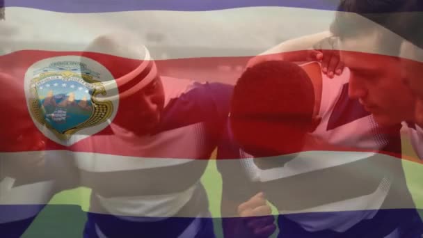 ハドルデジタル構成で多民族の男性ラグビーチームに手を振るコスタリカの旗のアニメーション — ストック動画