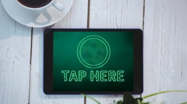 Yeşil neon renkli kelimelerin animasyonu Tap Here, bir masanın üzerine koyulmuş dijital tabletin ekranında titreşiyor bir fincan kahveyle. İletişim ve bağlantı konsepti dijital olarak oluşturuldu.