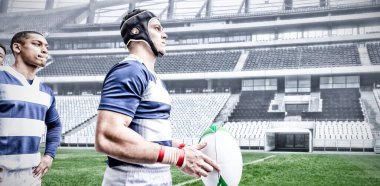 Çok ırklı rugby oyuncularından oluşan takım bir spor stadyumunda rugby oynuyor, takım elbisesi giyiyor, elinde bir top, dijital bir kompozit tutuyor..