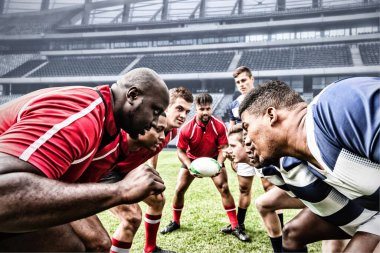 İki çok ırklı rugby oyuncusu bir spor stadyumunda rugby oynuyorlar, takım elbisesi giyiyorlar, birbirlerine bakıyorlar, bir oyuncu rugby topu tutuyor..