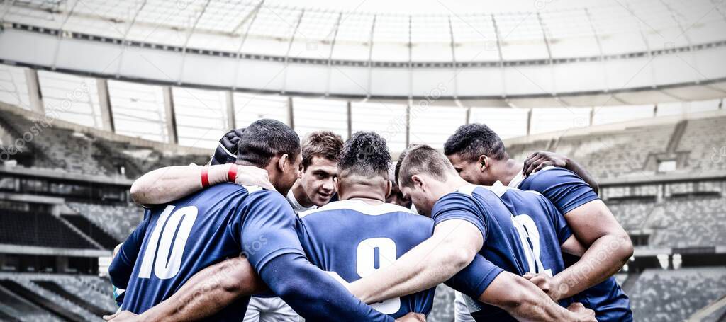 Team of multi-ethnic rugby players playing rugby at a sports stadium, wearing team strip, standing in a huddle, motivating before a game, digital composite.