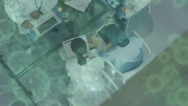 病院の机の上に座っている男性と女性の医療従事者の高い角度のビューに浮かんでいるマクロCovid 19細胞のアニメーション コロナウイルスCovid 19パンデミックコンセプトデジタル複合体 — ストック動画