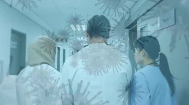 Hastanede dolaşan üç çok ırklı kadın ve erkek sağlık çalışanının dikiz aynasından süzülen makro covid-19 hücrelerinin animasyonu. Coronavirus Covid-19 pandemik konsept dijital bileşik