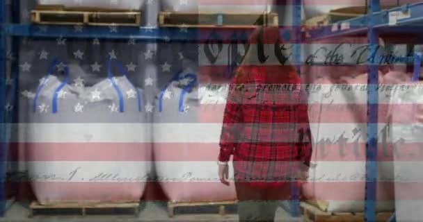 背景にある倉庫で働く女性に対するアメリカの憲法のテキストで手を振るアメリカの国旗のアニメーション アメリカ社会の発展愛国心の概念デジタル構成 — ストック動画
