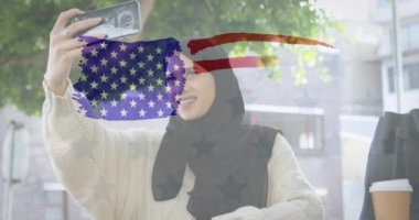 Amerikan bayrağının animasyonu arka planda akıllı telefonuyla özçekim yapan tesettürlü melez kadın üzerine çizilmiş. Amerikan toplumu çeşitlilik kavramı dijital kompozisyon.