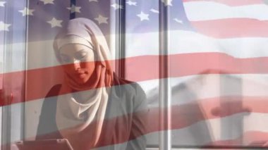 Arka planda dijital tablet kullanarak tesettürlü melez kadın üzerinde dalgalanan Amerikan bayrağının animasyonu. Amerikan toplumu çeşitlilik kavramı dijital kompozisyon.