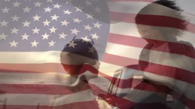 Sahilde bayrak sallayan Amerikan bayrağının animasyonu. Sahilde yaz tatili yolculuğunda arka planda karışık ırk çifti. Amerikan toplumu çeşitlilik kavramı dijital kompozisyon.