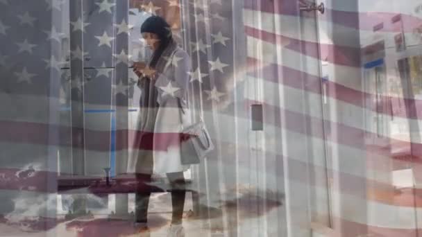 背景にはスマートフォンを使い ヒジャーブ州で混在した人種の女性に手を振るアメリカ国旗のアニメーション アメリカ社会の多様性の概念デジタル組成 — ストック動画