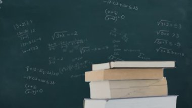 Arkadaki yeşil karatahta üzerindeki kitapların üzerinde hareket eden matematiksel formüllerin animasyonu. Eğitim kavramının dijital ortamda çözülmesi sorunu.