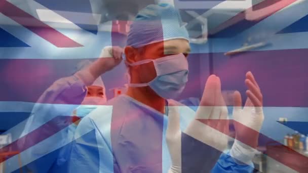 Animación Bandera Británica Ondeando Sobre Cirujano Ayudando Otro Poner Máscara — Vídeos de Stock