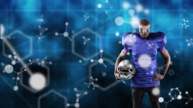 Erkek rugby oyuncusunun üzerinde hareket eden moleküler ve kimyasal yapıların dijital bileşik videosu mavi arkaplana karşı bir kask tutuyor.