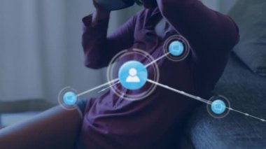 Sanal gerçeklik kulaklığı takarak evde bir kadının üzerinden veri transferi yapan insan simgelerinden oluşan bir ağın animasyonu. Dijital iletişim VR arayüz kavramı, dijital kompozit.