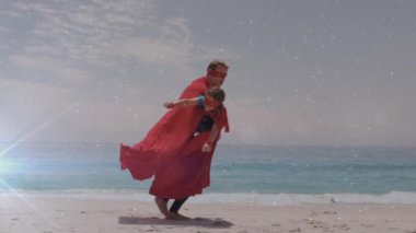 Sahilde oynayan süper kahraman kostümlü baba ve oğluna karşı beyaz, parlayan ışık noktasının dijital videosu.