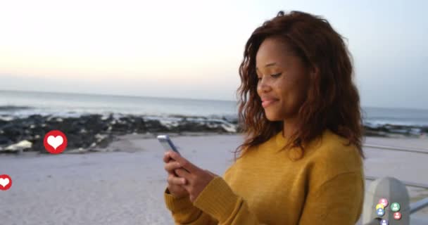 用智能手机和微笑在海滩上站着的女人上方飘扬的社交网络图标的动画 全球数字网络产生的图像 — 图库视频影像