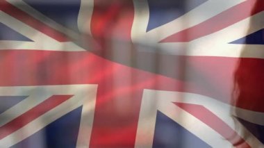 Yüz maskesi takmış, kameraya bakıp gülümseyen beyaz bir kadının üzerinde sallanan İngiliz bayrağı animasyonu. Covid-19 Coronavirus Ulusal Sağlık Güvenliği Konsepti Dijital Kompozit