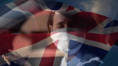 Yüz maskesi takan beyaz bir kadının üzerinde sallanan İngiliz bayrağı animasyonu. Covid-19 Coronavirus Ulusal Sağlık Güvenliği Konsepti Dijital Kompozit