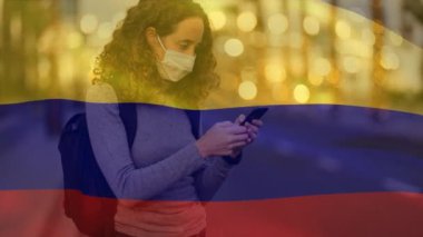 Kolombiya bayrağının beyaz kadın üzerinde sallanışının animasyonu. Yüz maskesi takıyor, akıllı telefon kullanıyor. Covid-19 Coronavirus Ulusal Sağlık Güvenliği Konsepti Dijital Kompozit