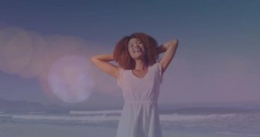 Sahilde kolları geniş mutlu melez bir kadının üzerinde hareket eden ışık lekelerinin canlandırması. Tatil ve rahatlama, dijital olarak üretilen video.