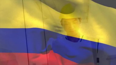 Kolombiya bayrağının elinde taslak olan kasklı, gülümseyen Asyalı erkek mimarın üzerinde dalgalanması. Kolombiya, işletme, mimari, tasarım ve geliştirme, dijital olarak üretilen video.