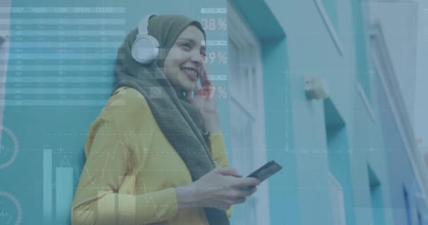 使用智能手机在Hijab中动画处理与Biracial妇女有关的财务数据 全球商业 计算和数据处理概念数字生成的视频 — 图库视频影像