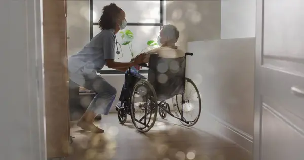 Image of bokeh over diverse doctor and patient sitting in wheelchair. Medicine, healthcare and lifestyle concept digitally generated image.