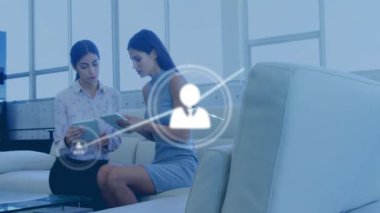 Tablet kullanan iki ırklı kadın meslektaşların üzerindeki ikonlarla olan bağlantıların animasyonu. Küresel iş ve dijital arayüz kavramı dijital olarak oluşturulmuş video.