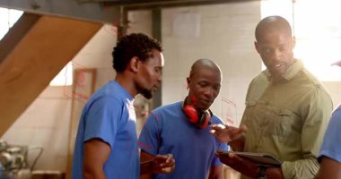 Supervisor in green shirt bringing digital plan on tablet while swiping and engaging workshop team. Collaboration, technology, manufacturing, teamwork, industrial, precision, training