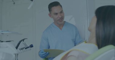 Önlük giymiş eldivenli dişçi tedavi odasında, dosya klasörlü, tepe lambalı tedaviyi açıklıyor. Klinik, profesyonel, sağlık, danışma, tanı, sterilizasyon, sağlık