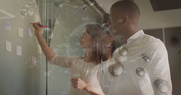 Коллеги маркируют заметки на стеклянной стене офиса красным маркером и цифровым накладыванием. работа, инновации, brainstorming, сотрудничество, офис, современность, данные