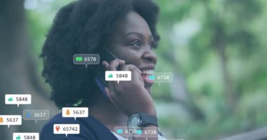 Animation of multiple social media icons over african american woman talking on smartphone outdoors. Social media networking and technology concept