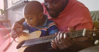 Mutlu Afro-Amerikan baba ve oğlunun gitar çalması üzerine parlayan ışığın animasyonu. Aile, ebeveynlik, müzik ve birlikte zaman geçirme konsepti dijital olarak oluşturulmuş video.