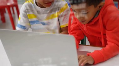 Kırmızı kapüşonlu çocuk, eğitime işaret eden çizgili çocuğu işaret ederken dizüstü bilgisayara el koyuyor. İşbirliği, takım çalışması, eğitim, gençlik, teknoloji, öğrenme, yenilik