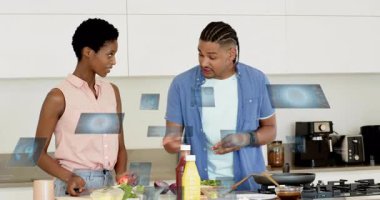 Erkek malzemelere el kol hareketi yaparken kadın yemek pişirmek için tavayı karıştırırken biber doğrar. Yemek pişirme, takım çalışması, yerli, aşçı, hazırlık, yaşam tarzı, modern