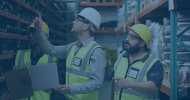 Miğfer takan işçiler depo koridorundaki stokları dizüstü bilgisayar ve not panosuyla kontrol ediyorlar. Sanayi, lojistik, takım, takım çalışması, organizasyon, verimlilik, depolama